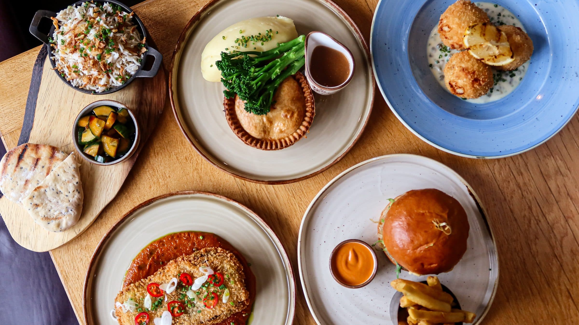 A table laid with pie and mash, fishcakes, burger and sides